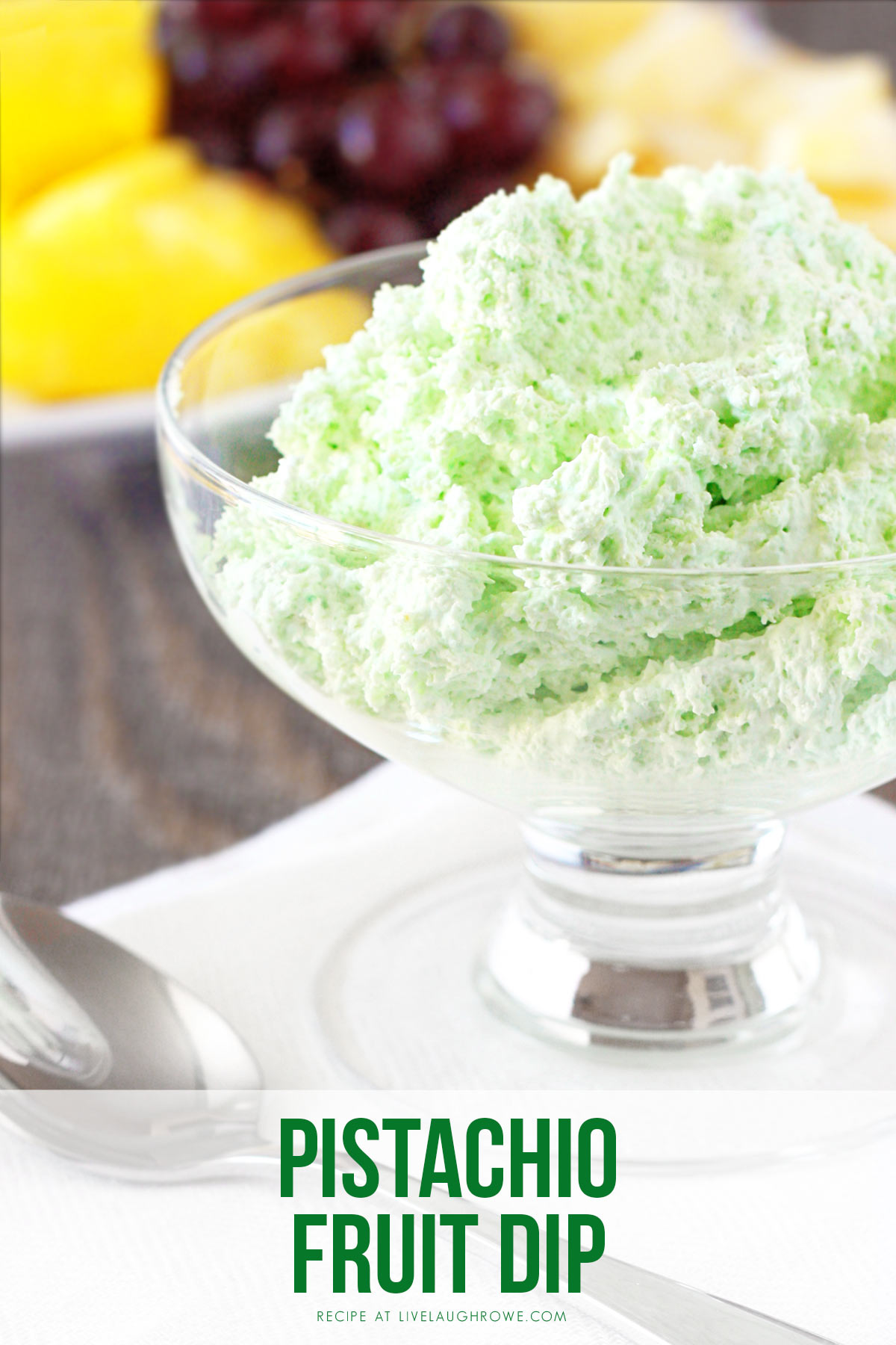 Light and fluffy pistachio fruit dip in a glass dessert bowl served with fresh fruit, perfect for St. Patrick&rsquo;s Day.