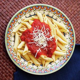 Overhead view of penne pasta topped with homemade pasta sauce and shredded Parmesan cheese.