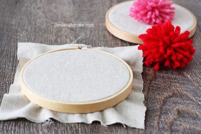 Add a pom pom to fabric in an embroidery hoop for some embroidery hoop art fun