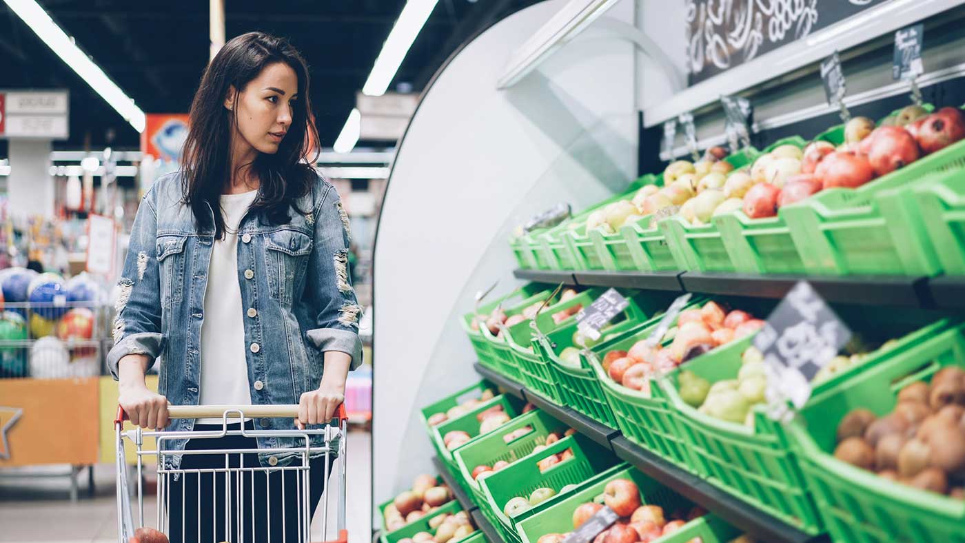 Woman grocery shopping with a cart in the produce aisle, showing everyday habits that help increase daily step count.