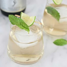 Close-up of a Hugo Spritz cocktail with ice, fresh mint, and a lime garnish.
