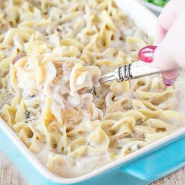 Creamy tuna casserole with egg noodles in a white baking dish, served with green peas on the side.