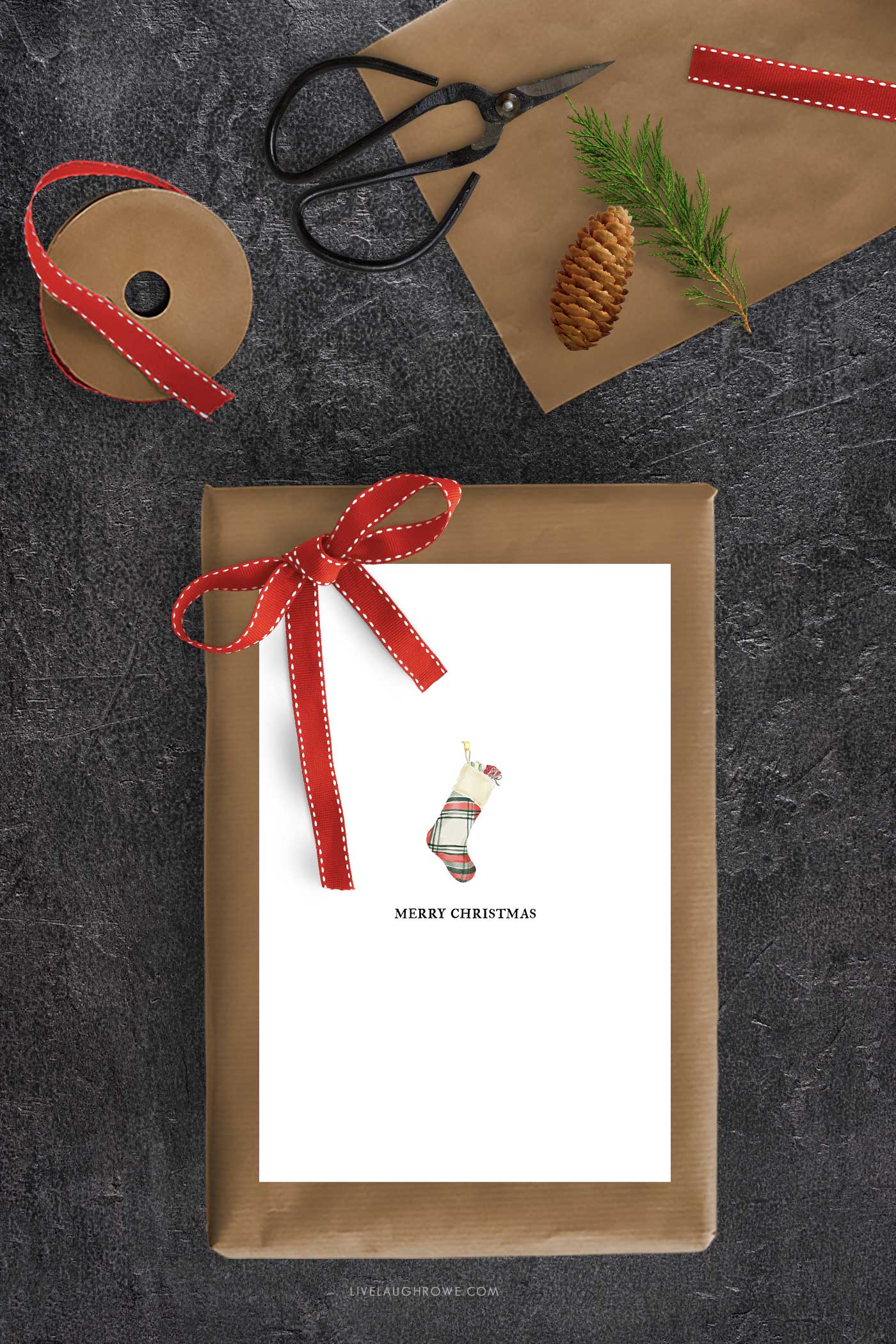 Kraft-wrapped Christmas gift tied with red ribbon topped with a plaid stocking printable Christmas card