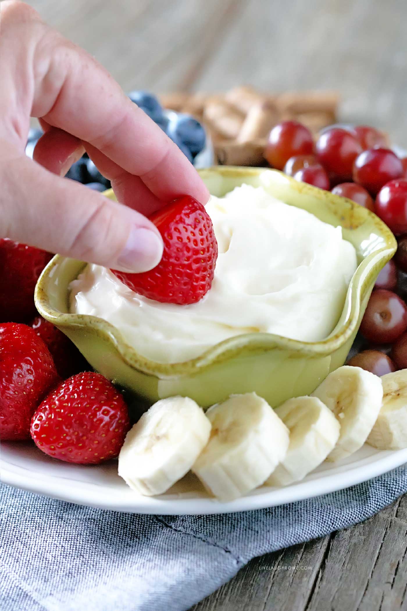 Hand Dipping Strawberry into Marshmallow Cream Cheese Fruit Dip
