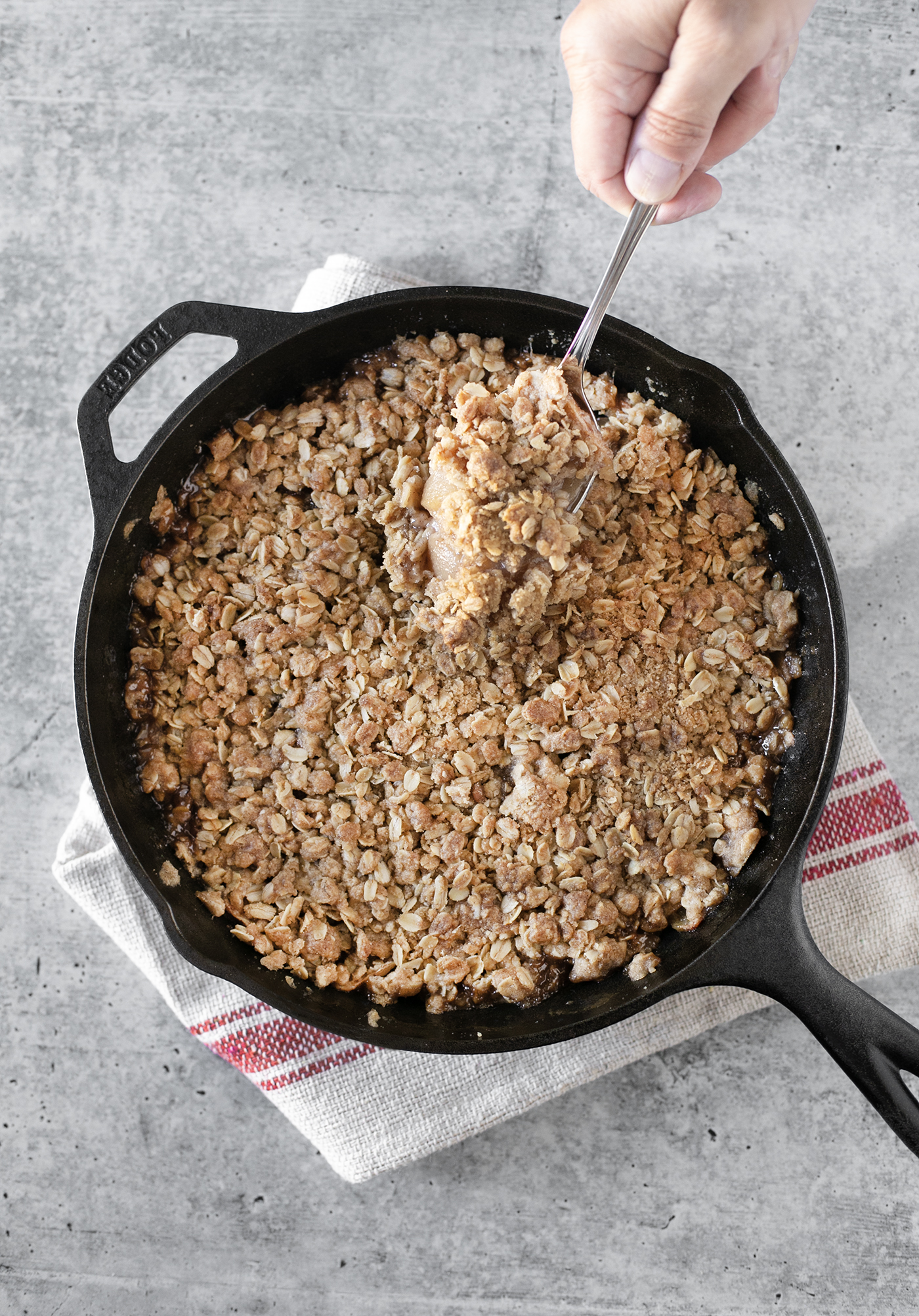 Scooping out the apple crisp from cast iron pan