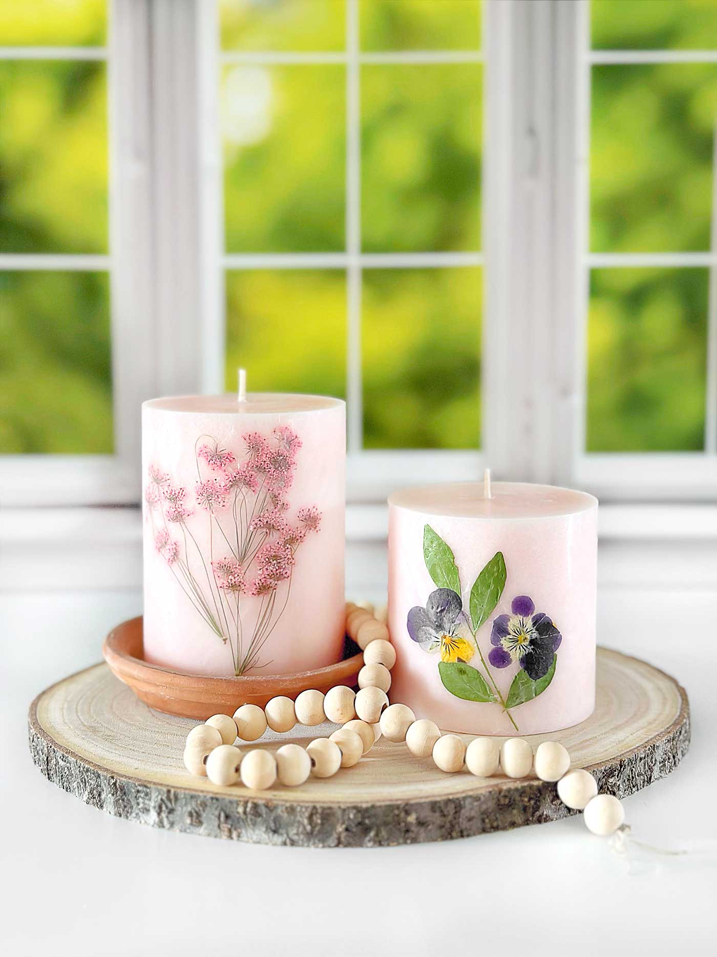 pink candles with pressed flowers styled on slice of wood