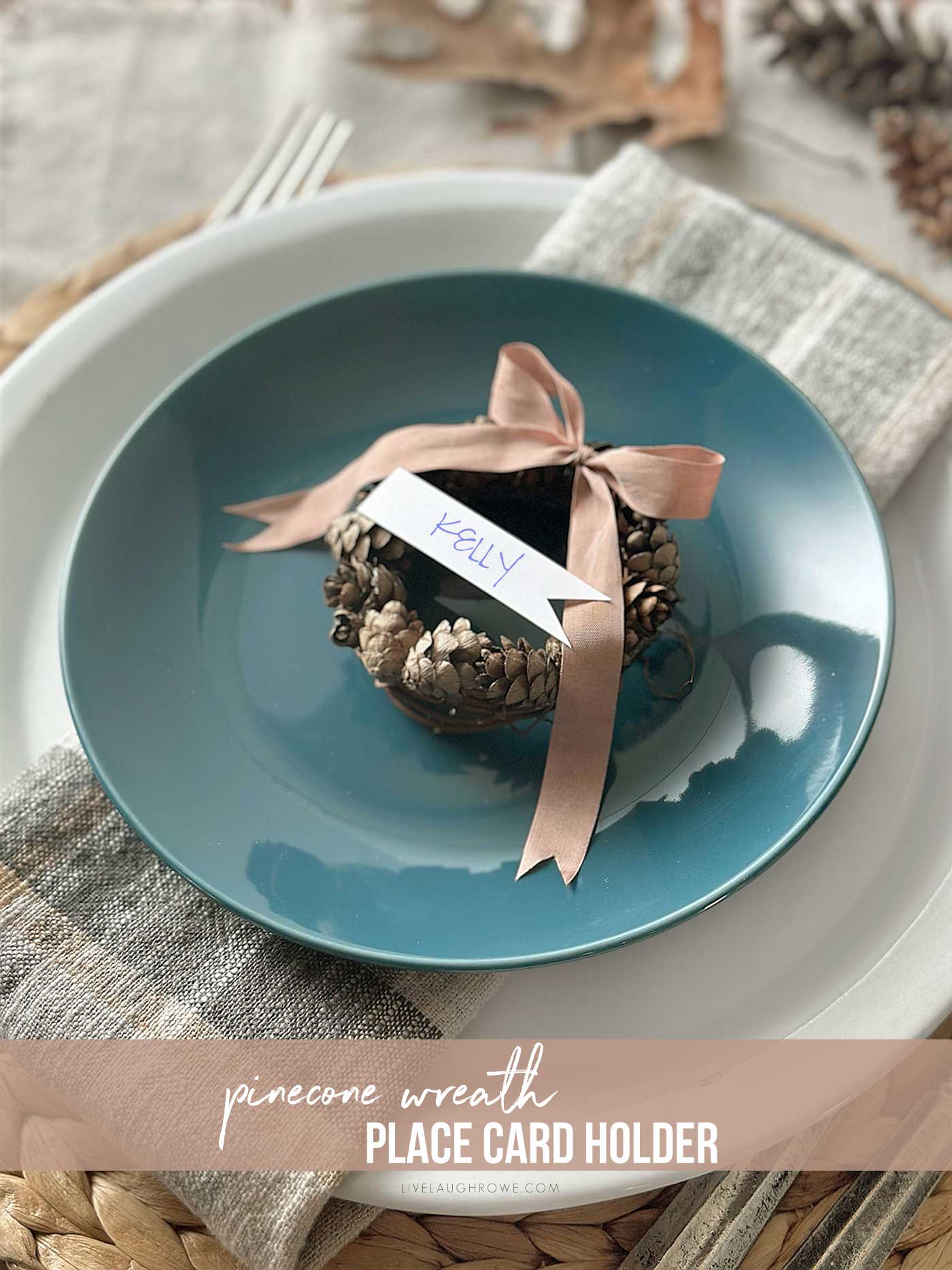 fall placesetting with grapevine wreath, pine cones, a ribbon all sitting on a blue place on top of a fall plaid napkin