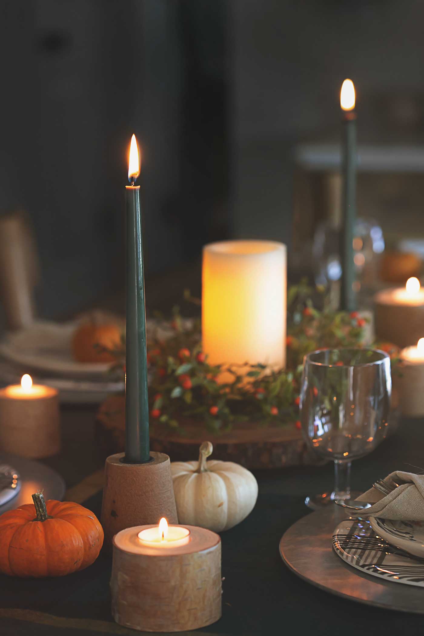 lit candles, pumpkins, plates on a table for thanksgiving celebration