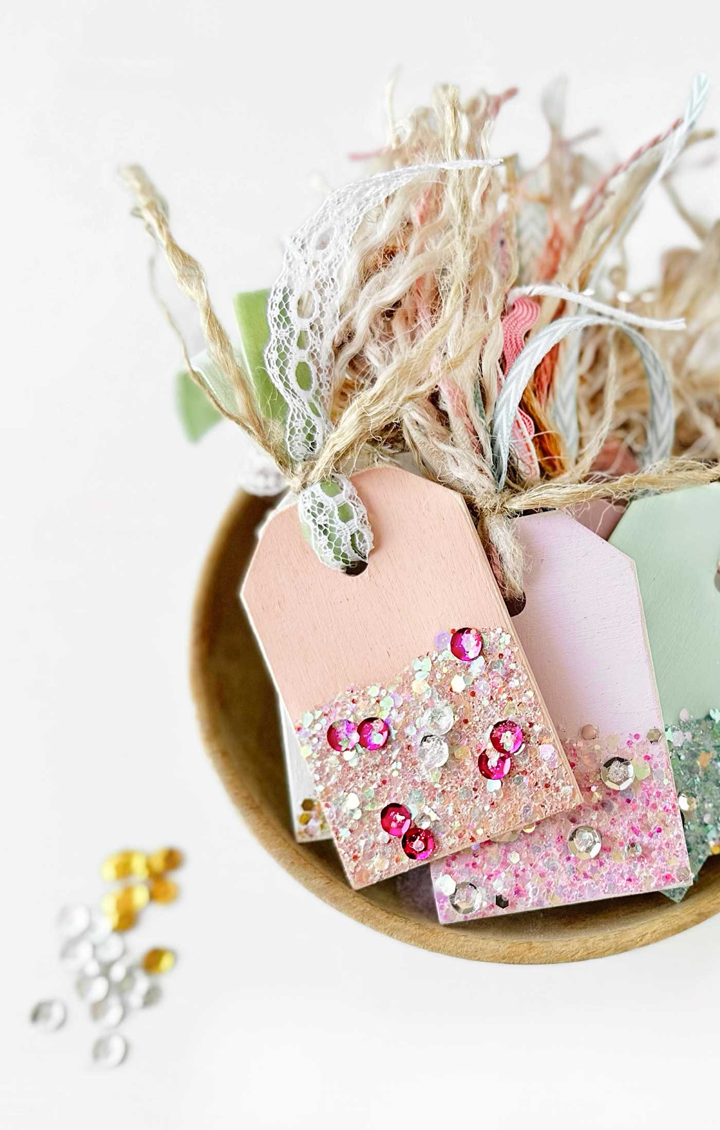 Lots of sparkle on these gift tags pictured in a bowl with ribbon tied to them.