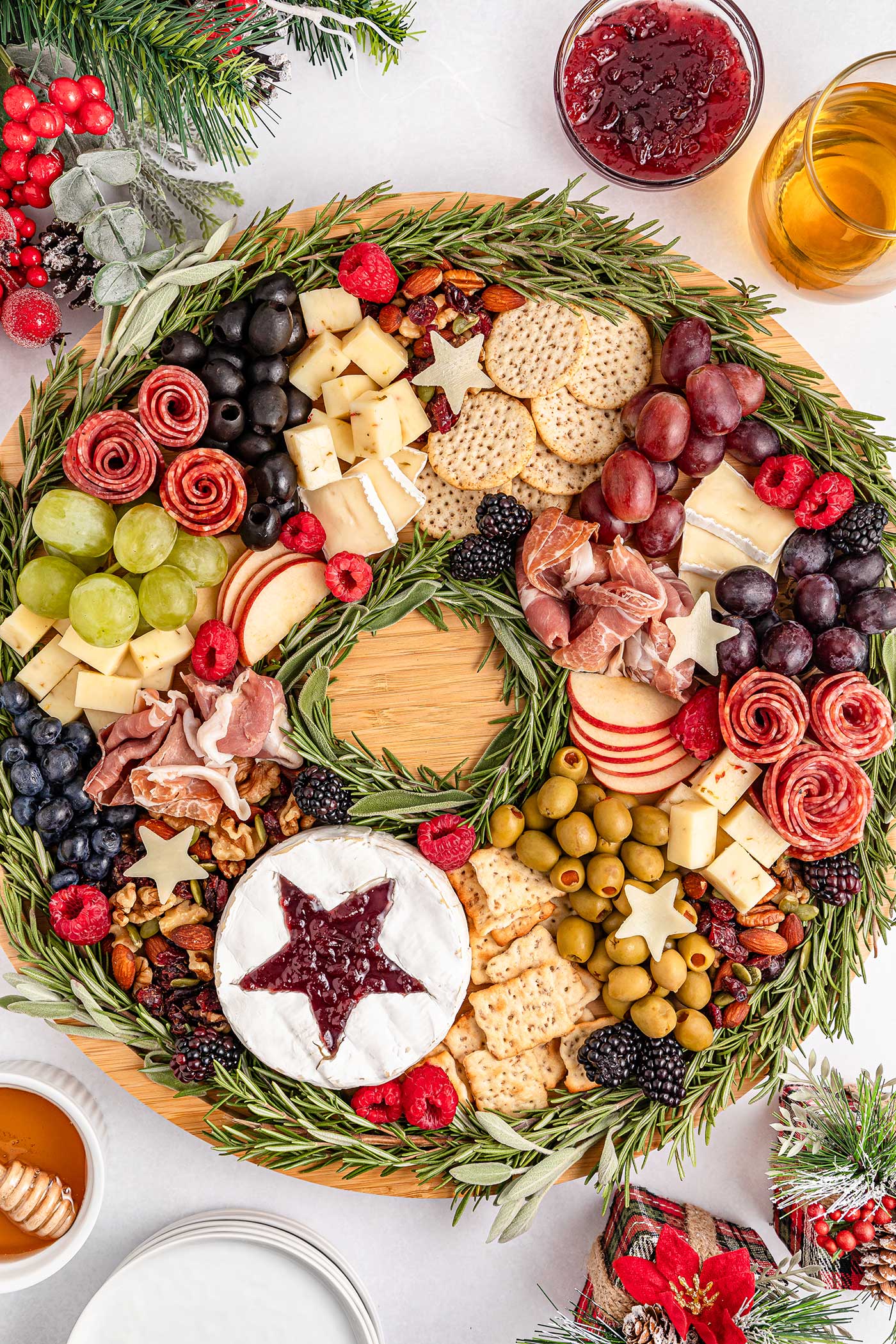 Round cutting board full of meats, cheese, crackers, fruits, nuts and olives. Holiday Charcuterie Board.