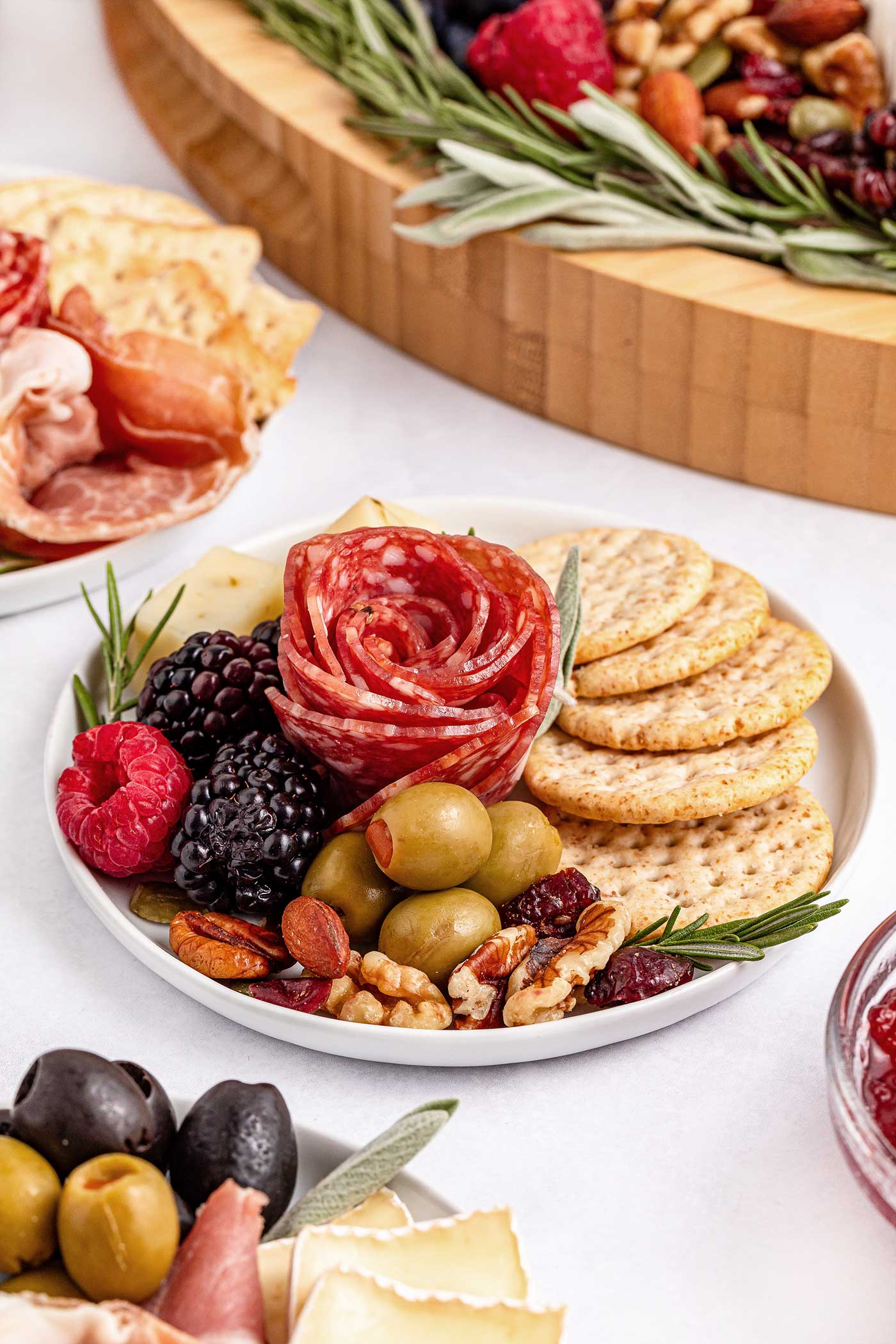 small white plate of charcuterie goodies such as a pepperoni rose, crackers, olives, and berries