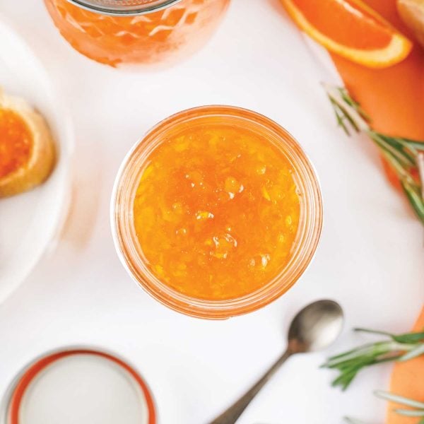 jar of orange marmalade in a glass jar with a spoon laying beside it