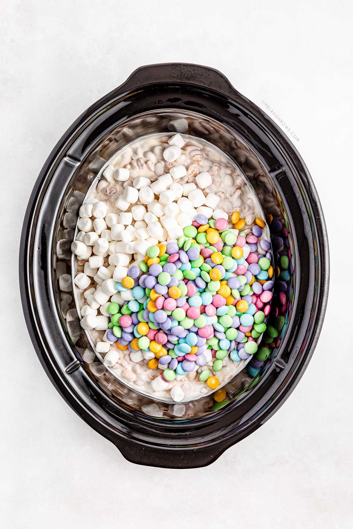 adding marshmallows and M&M's to the slow cooker