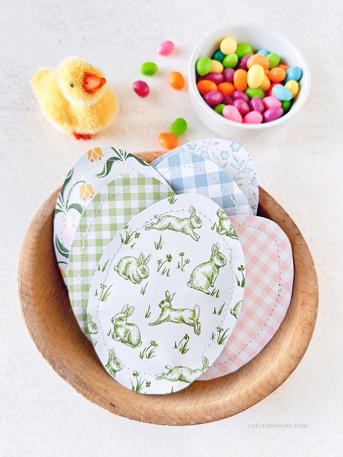 Wood bowl of paper easter eggs with a small bowl of jelly beans and a baby chick