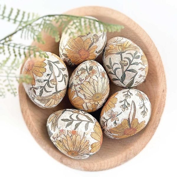 decoupage easter eggs in a wooden bowl with fern fronds hanging over it