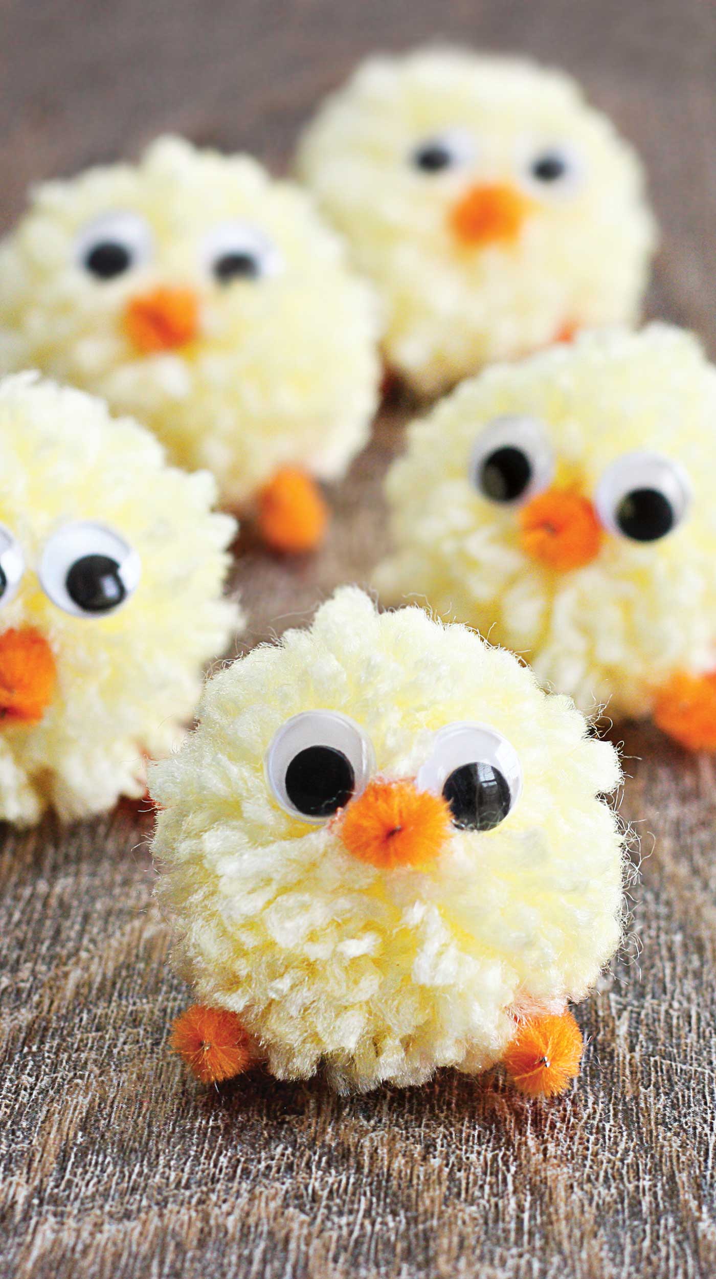 Pom Pom Chicks lined up looking adorable with googly eyes and pipe cleaner beak