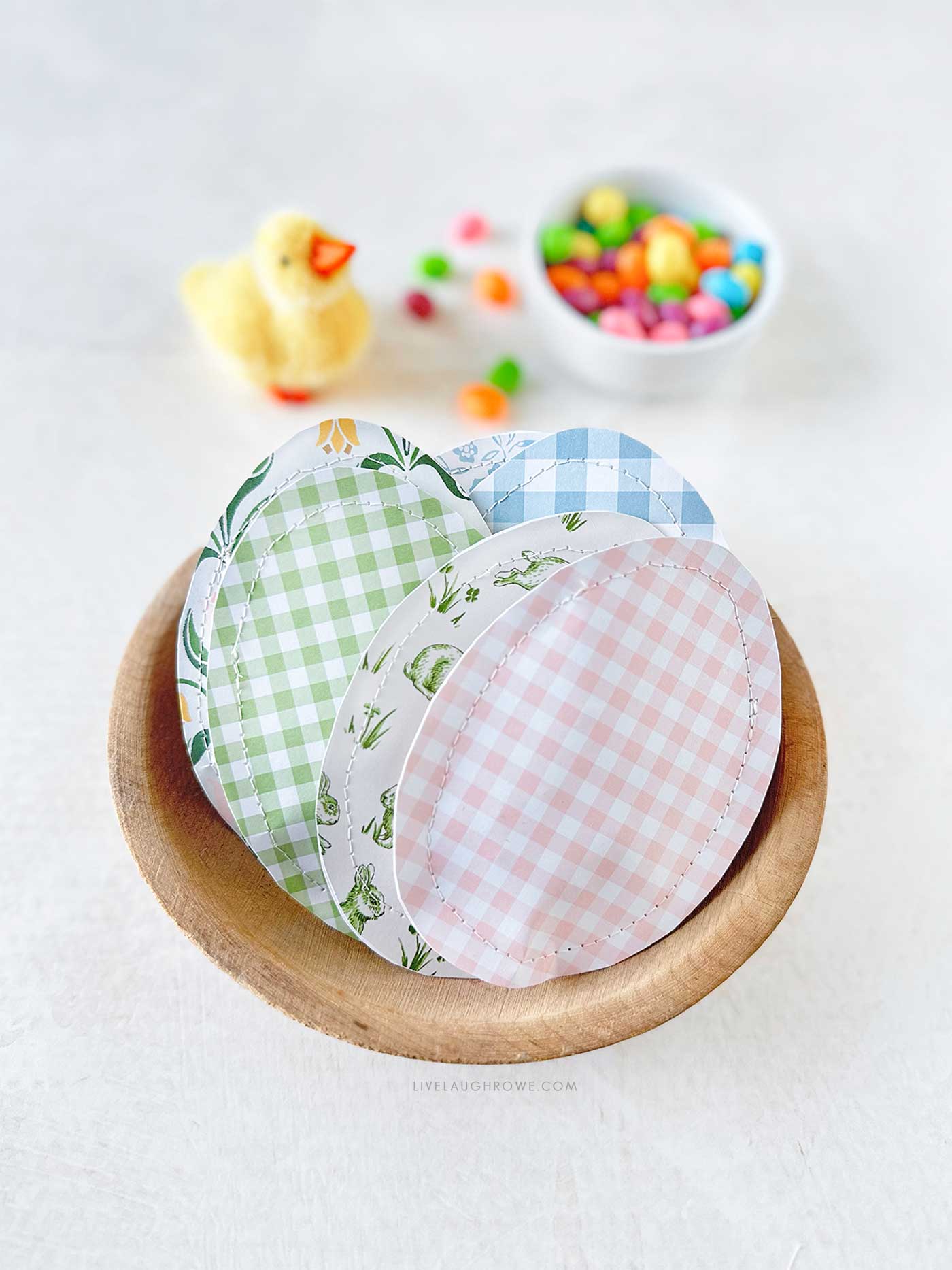 Wood bowl of paper sewn eggs with a small bowl of jelly beans and a baby chick