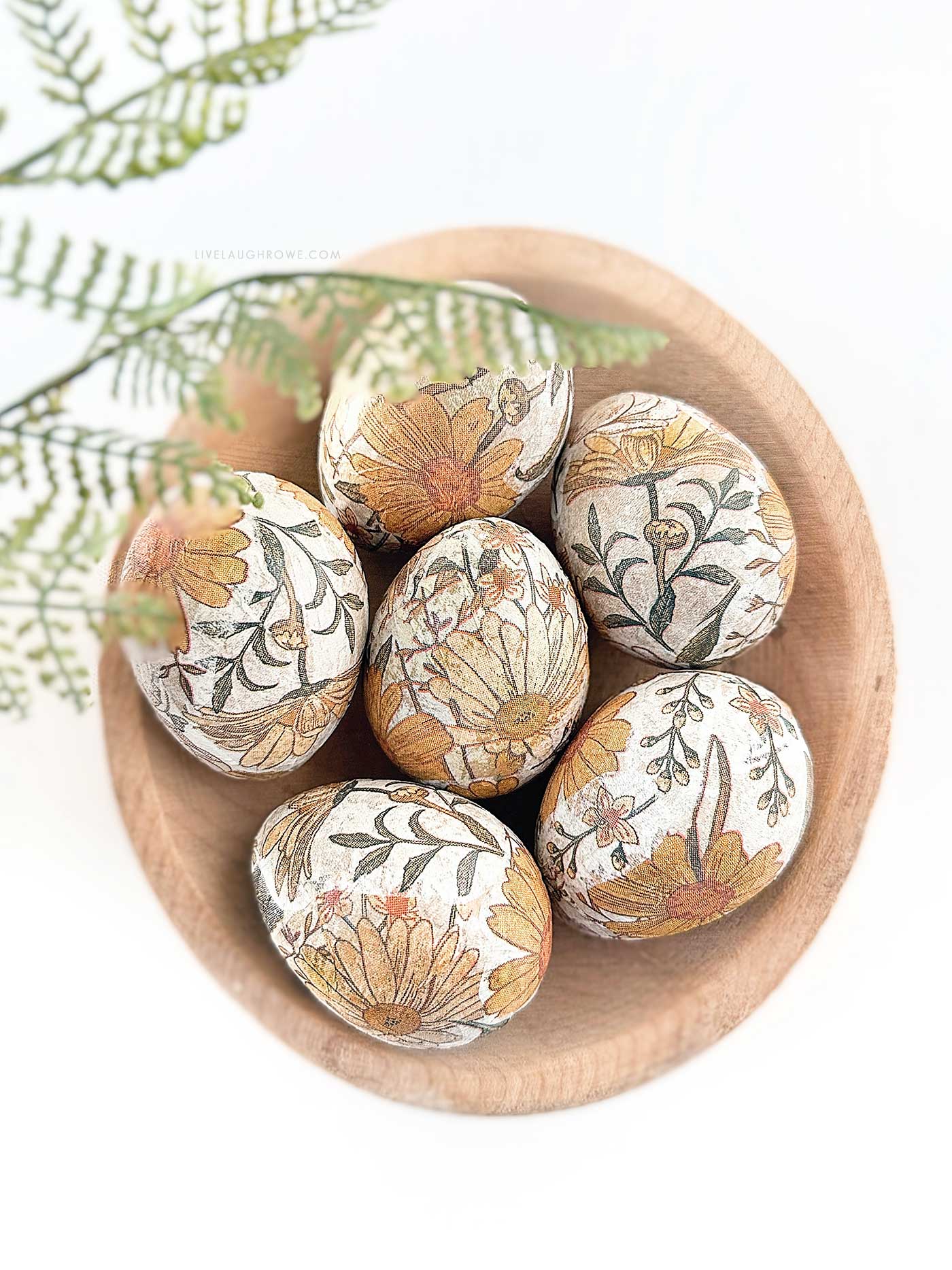 decoupage easter eggs in a wooden bowl with fern frond hanging over it