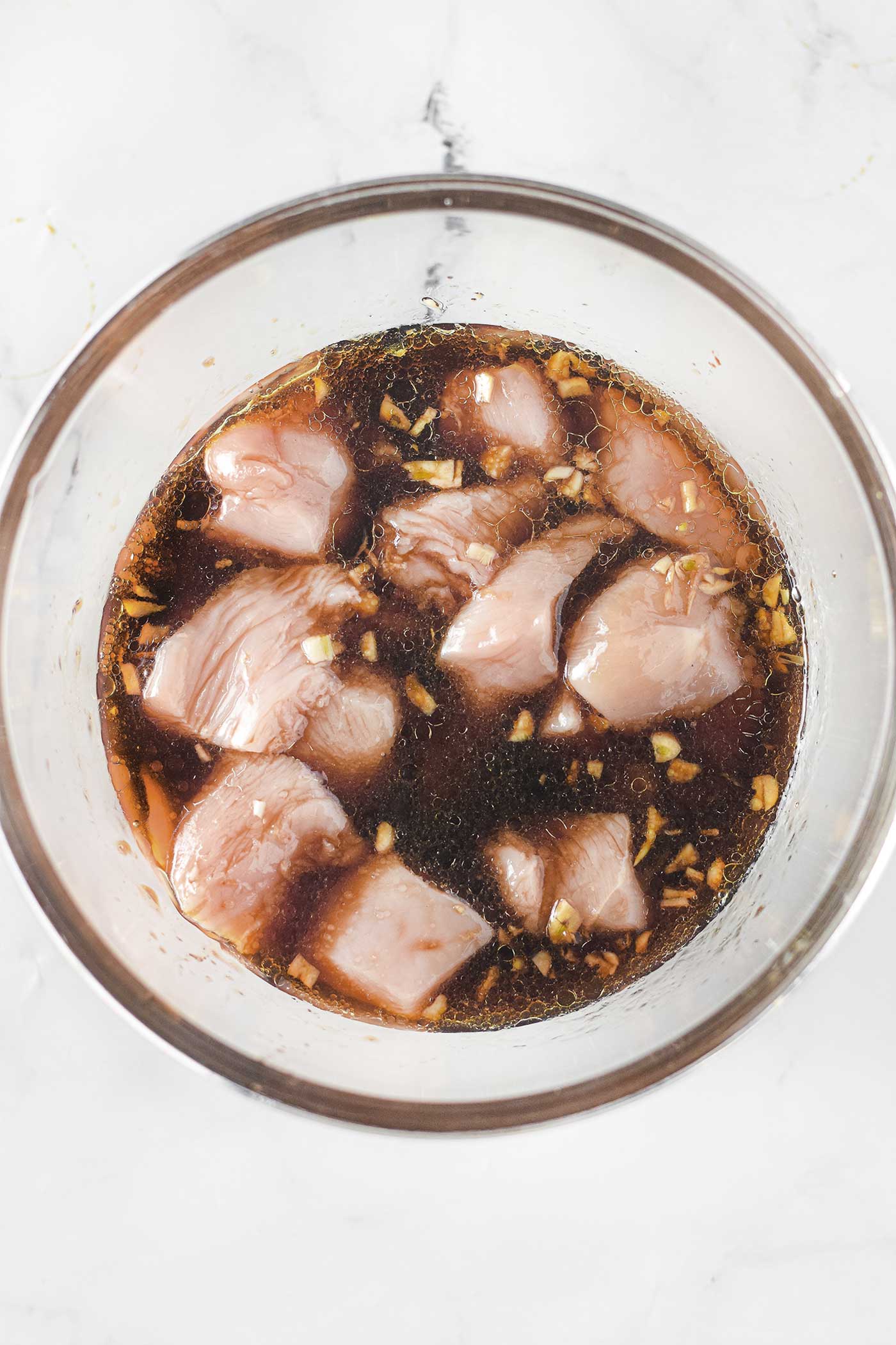 bowl of cut up chicken marinading in teriyaki sauce