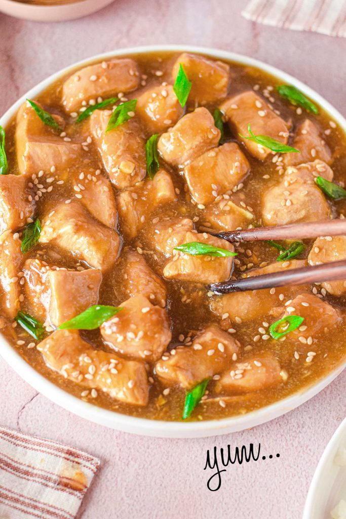 up close picture on chopsticks picking up a piece of chicken with sauce