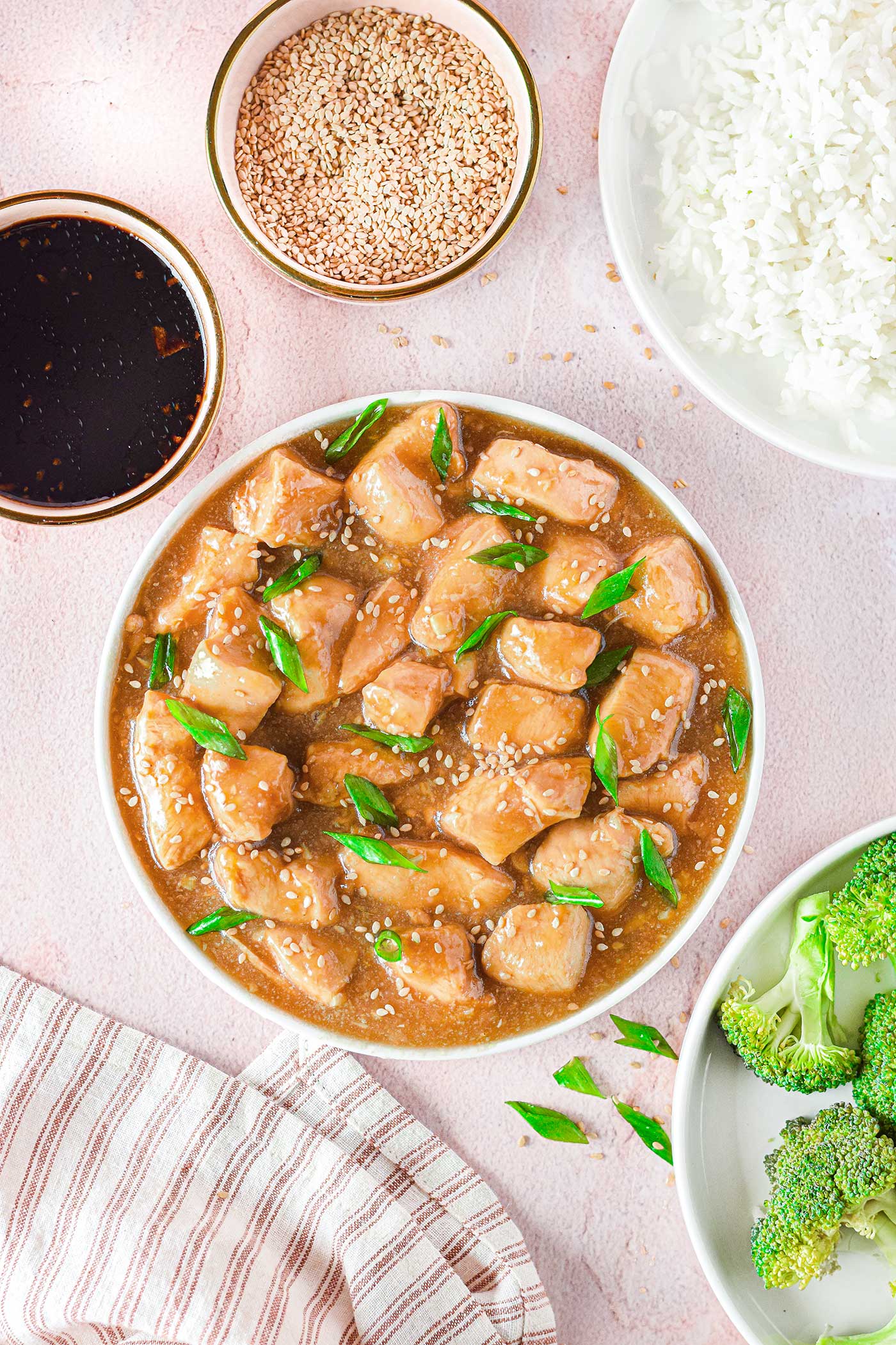 multiple prep bowls filled with ingredients and a bowl of teriyaki chicken with green onions and sesame seeds sprinkled on top