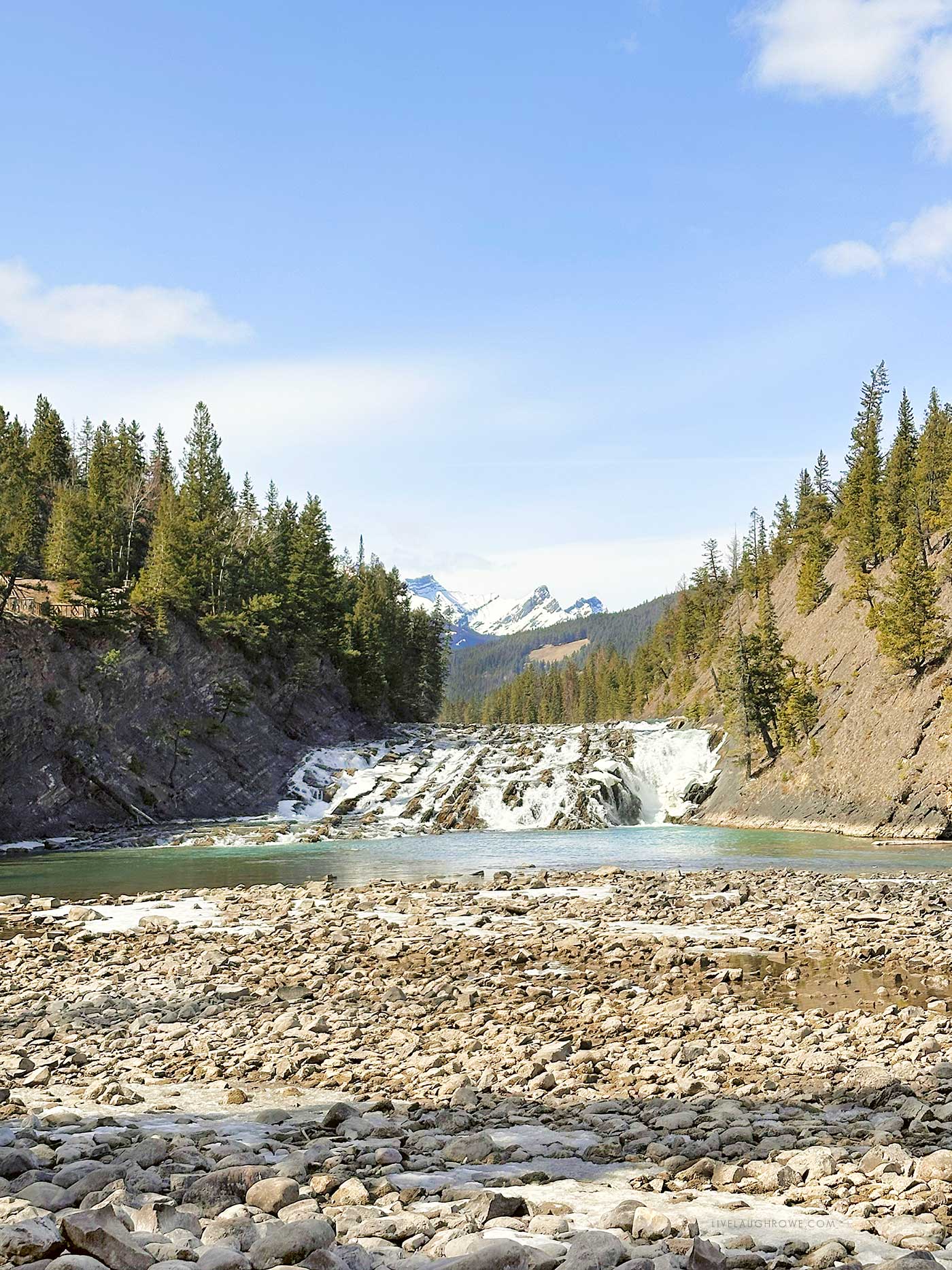 waterfall between mountain peaks with the white capped Canadian Rockies in the background.