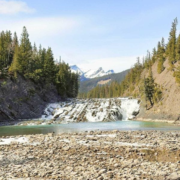 waterfall between mountain peaks with the white capped Canadian Rockies in the background.