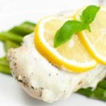 square image with a green vegetable, chicken breast with sauce topped with lemon slices on a white plate
