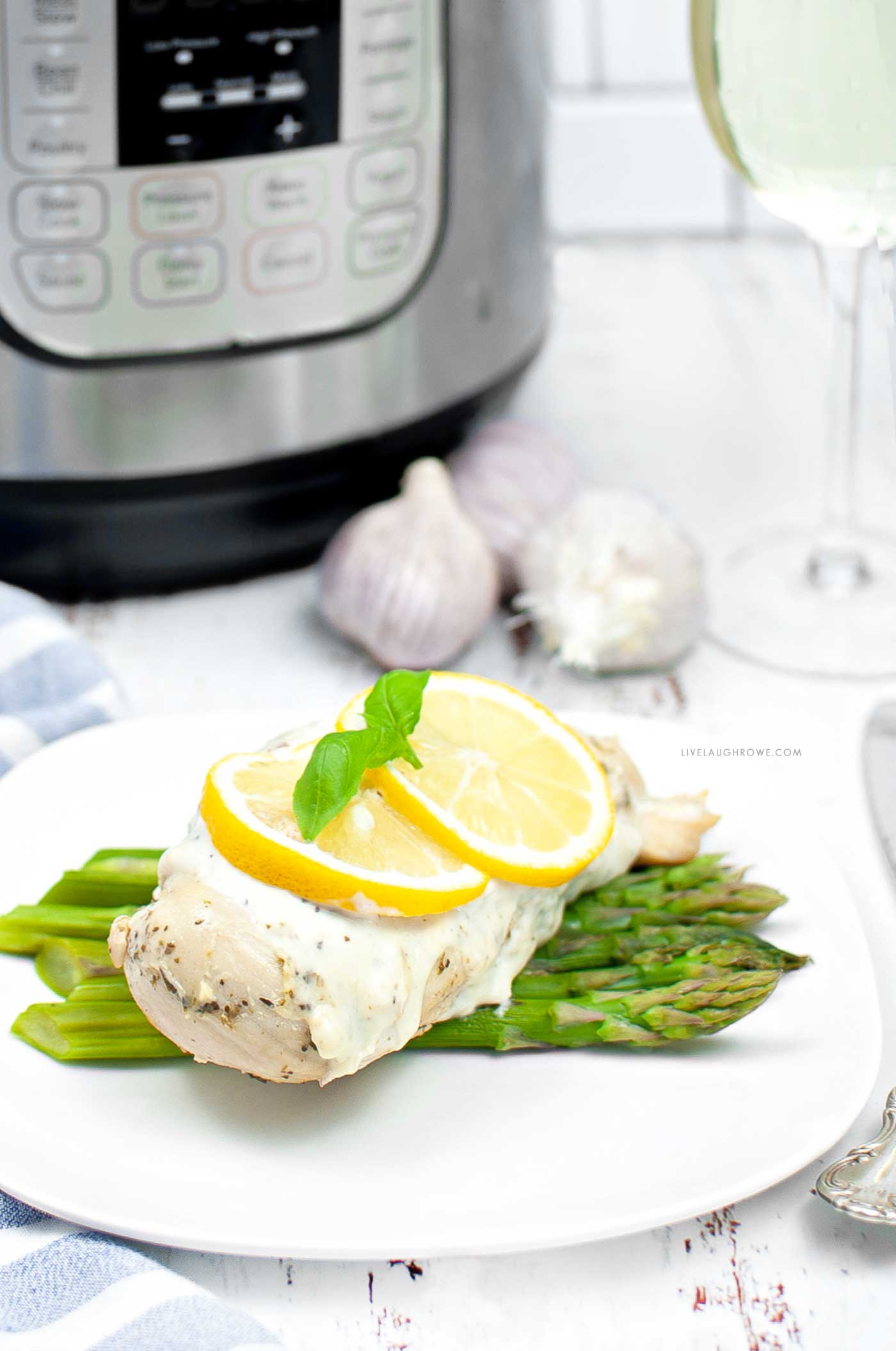 creamy lemon chicken plated over asparagus with garlic, an instant pot and a glass of white wine in the background.