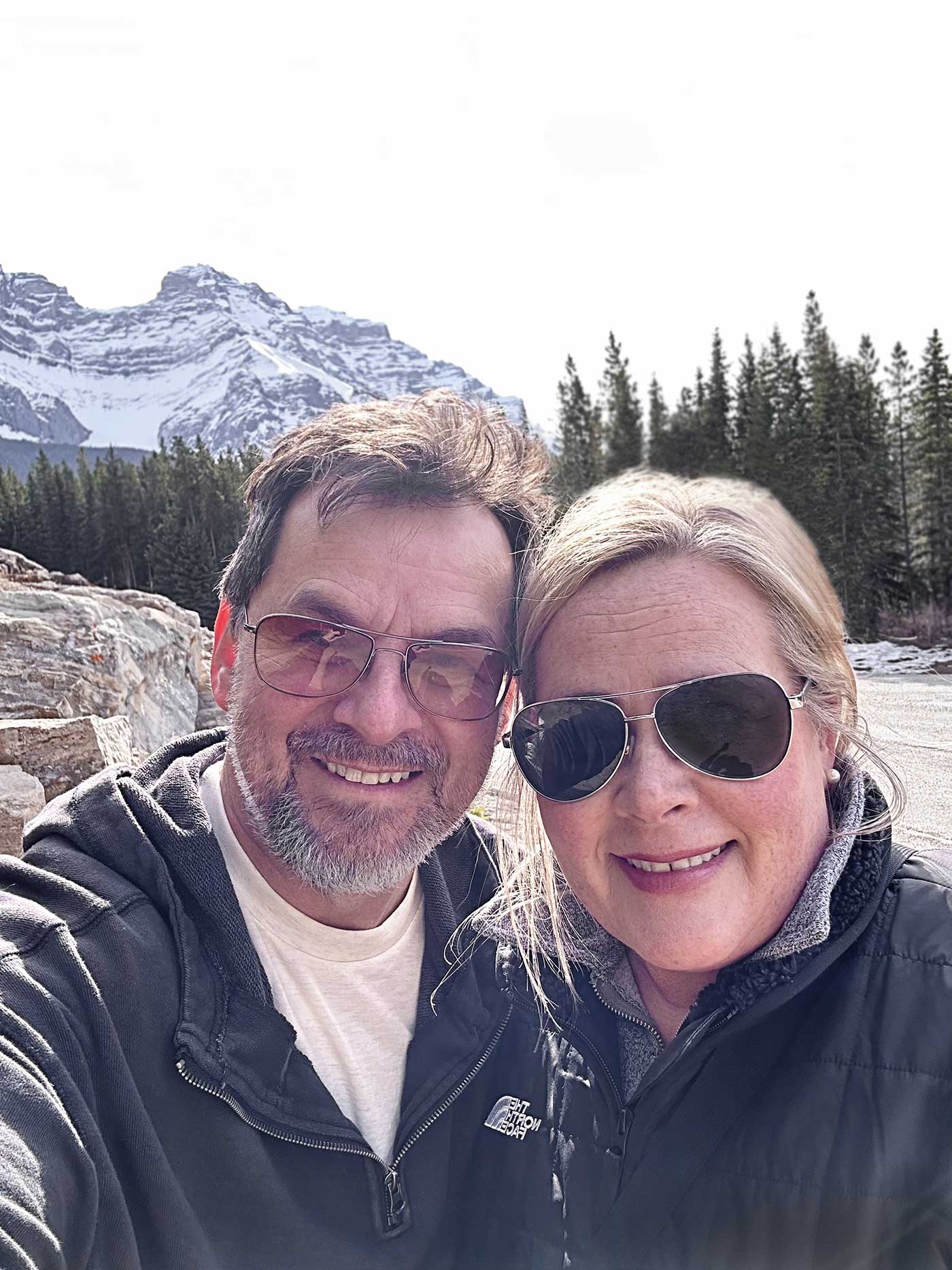 middle aged couple take a selfie with mountains and trees as the background