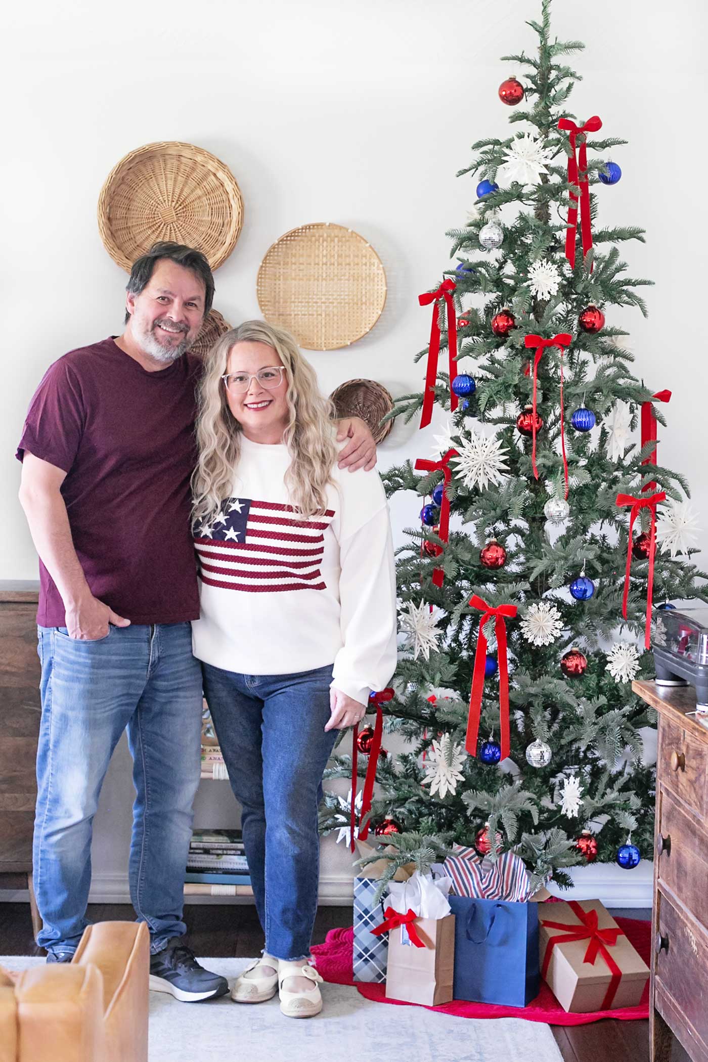 Smiling couple standing beside a tree decorated for Christmas in July, celebrating a July 4th birthday with red, white, and blue decorations.
