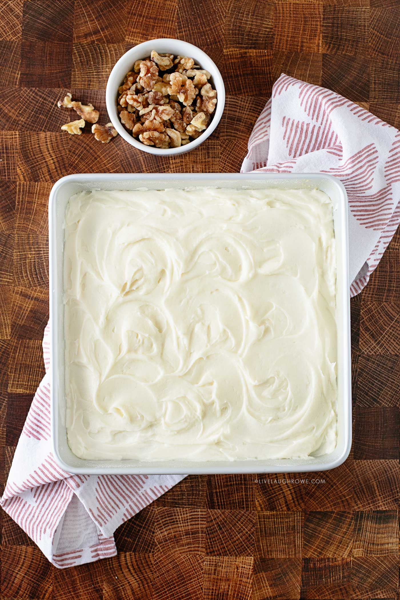 Carrot cake photographed from overhead with the Cream Cheese Frosting being the star of the show. A bowl of walnut on the side.