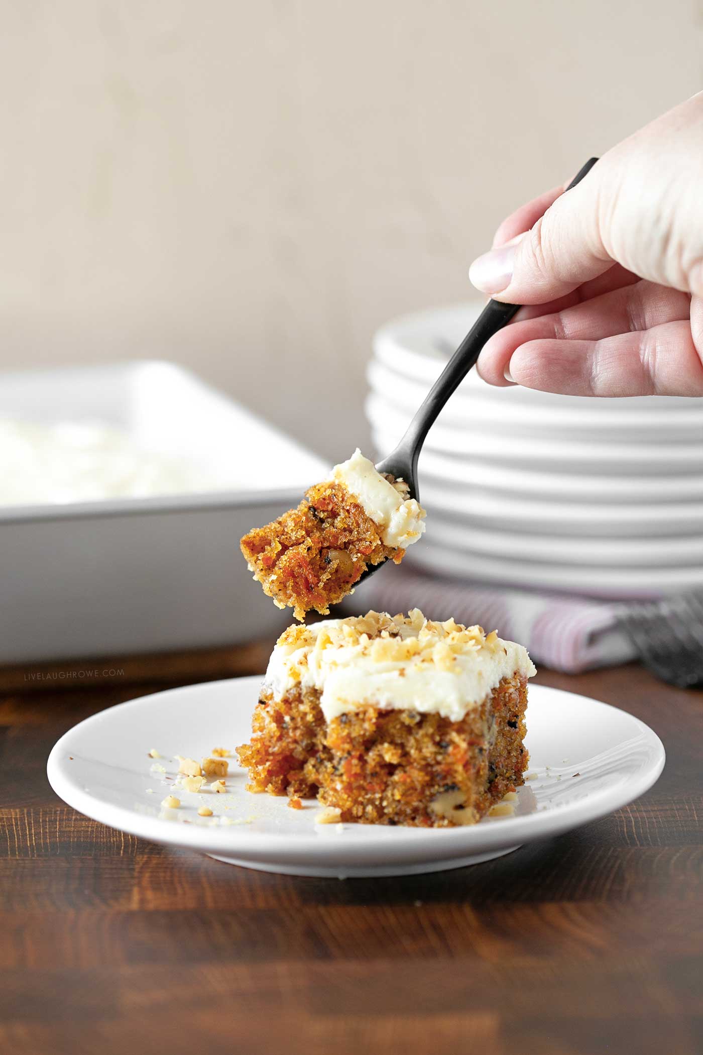 hand holding a fork and taking a small piece of cake from the slice of carrot cake