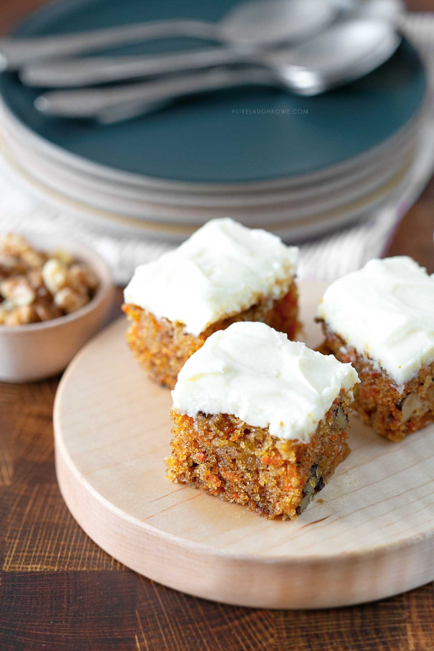 carrot cake bites. small pieces of carrot cake on a wooden stand with plates and silverware in the background