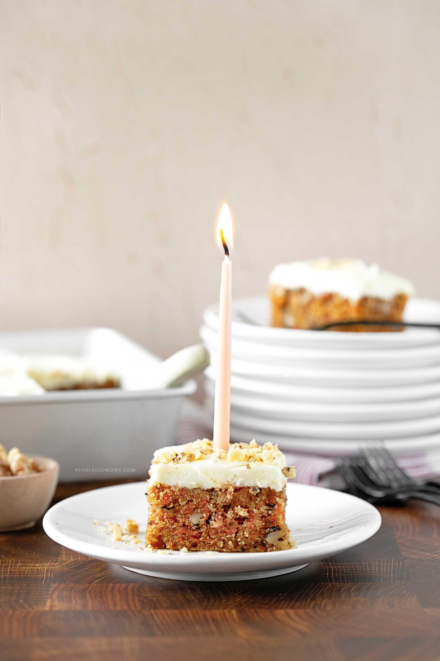 slice of cake with a lit candle placed in it. butcher block surface with plates and cake pan in the background