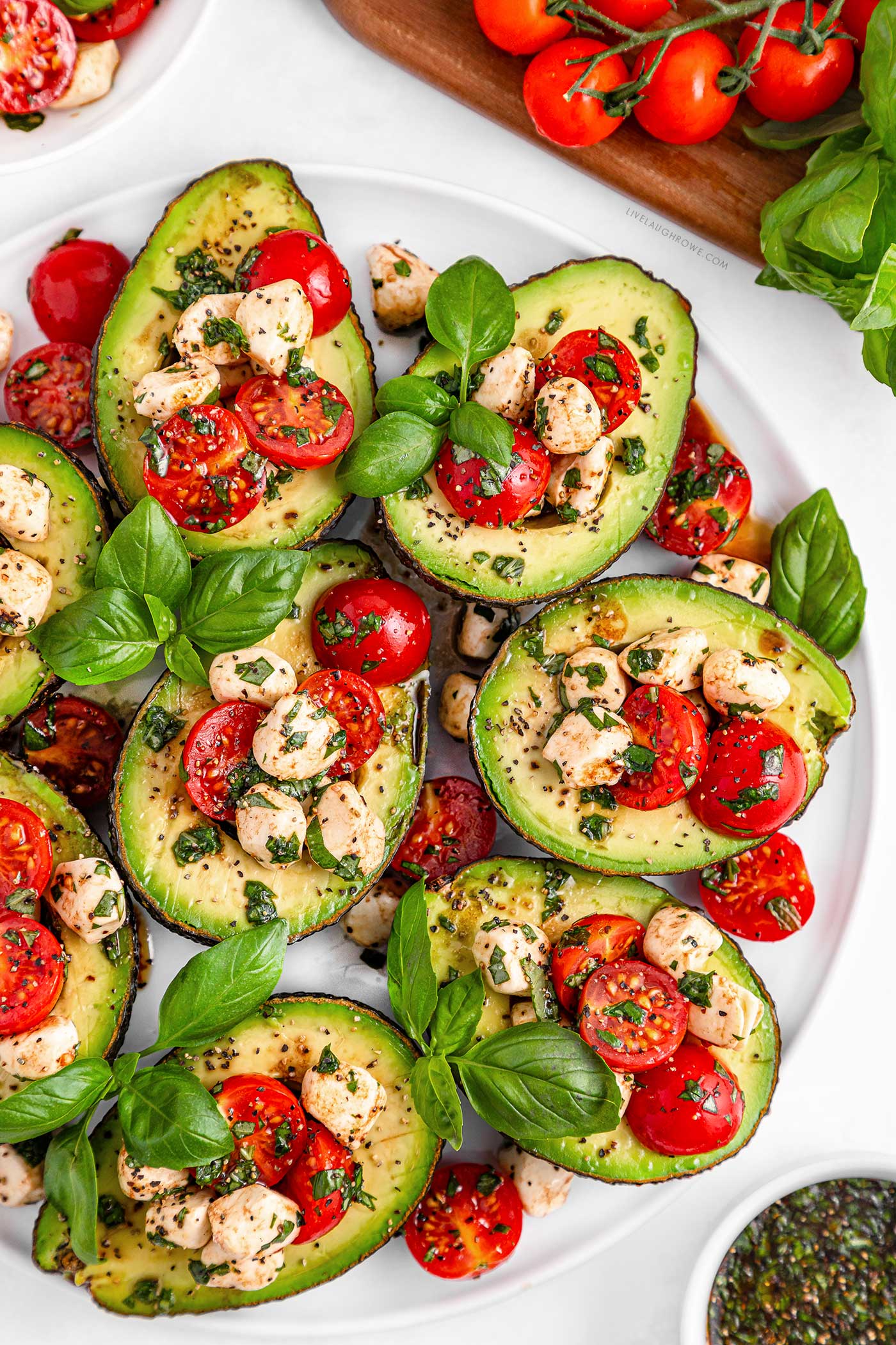 white plate on a white background with caprese stuffed avocados and basil for garnish