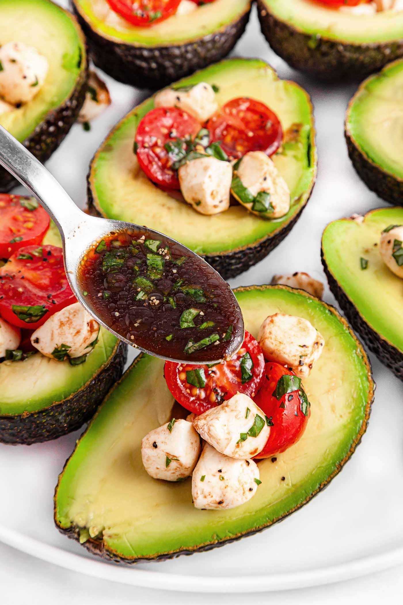spoon drizzling extra dressing over avocados
