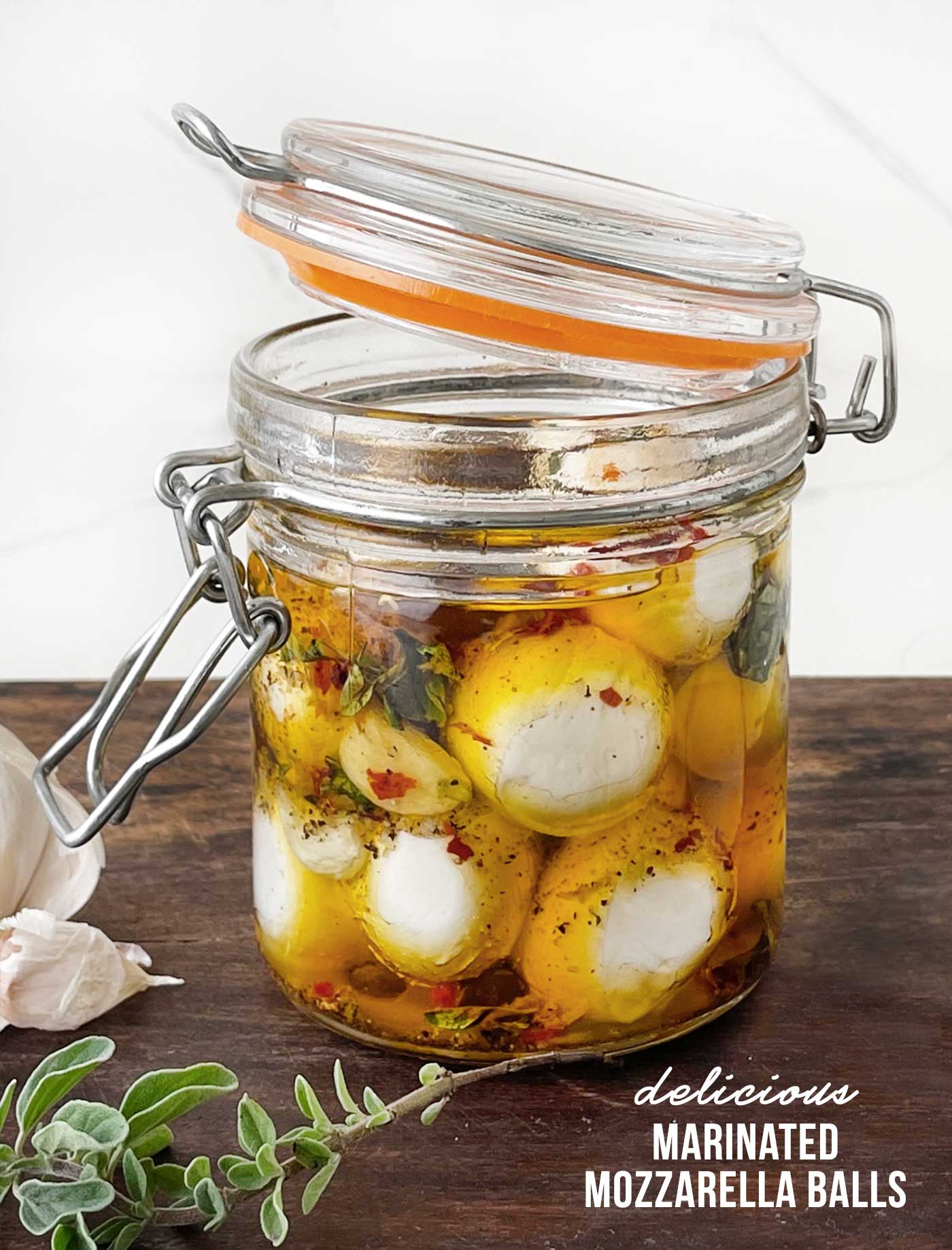 Close-up of fresh mozzarella balls soaking in a flavorful herb and olive oil marinade inside a sealed glass jar.