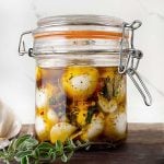 Close-up of fresh mozzarella balls soaking in a flavorful herb and olive oil marinade inside a sealed glass jar.