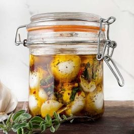 Close-up of fresh mozzarella balls soaking in a flavorful herb and olive oil marinade inside a sealed glass jar.