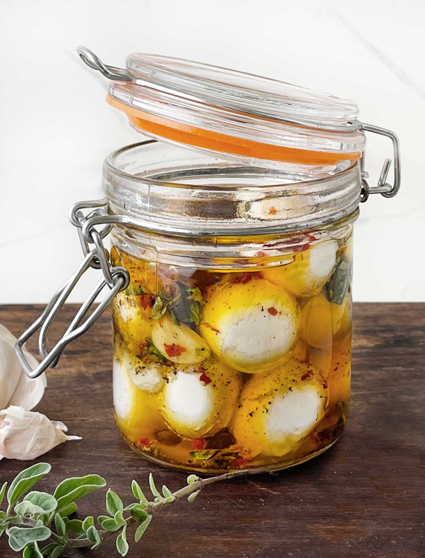 Close-up of fresh mozzarella balls soaking in a flavorful herb and olive oil marinade inside a sealed glass jar.