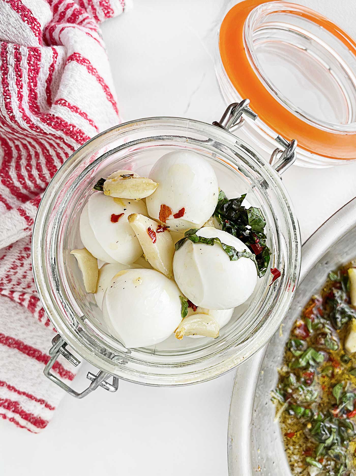 adding spices into a jar filled with bite-sized mozzarella balls