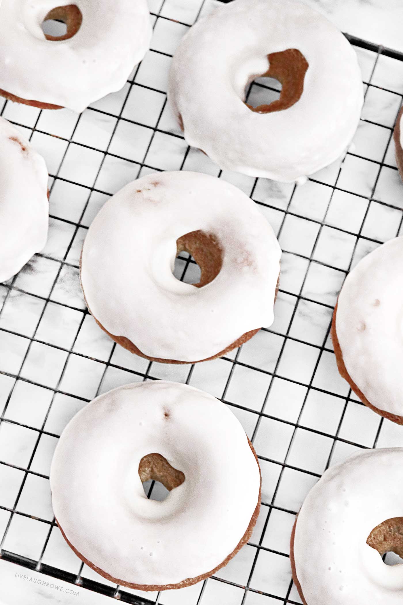 Freshly baked Orange Spice Donuts cooling on a wire rack with glaze dripping.