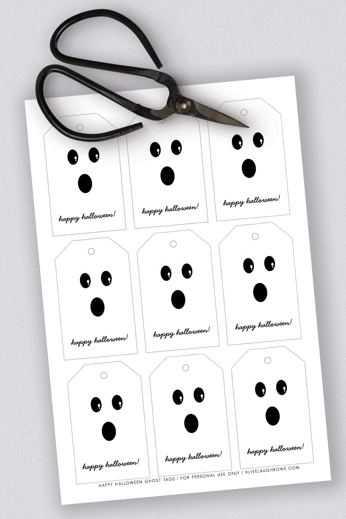 A printable sheet of simple black-and-white Halloween tags with cute ghost faces and scissors laying beside them.