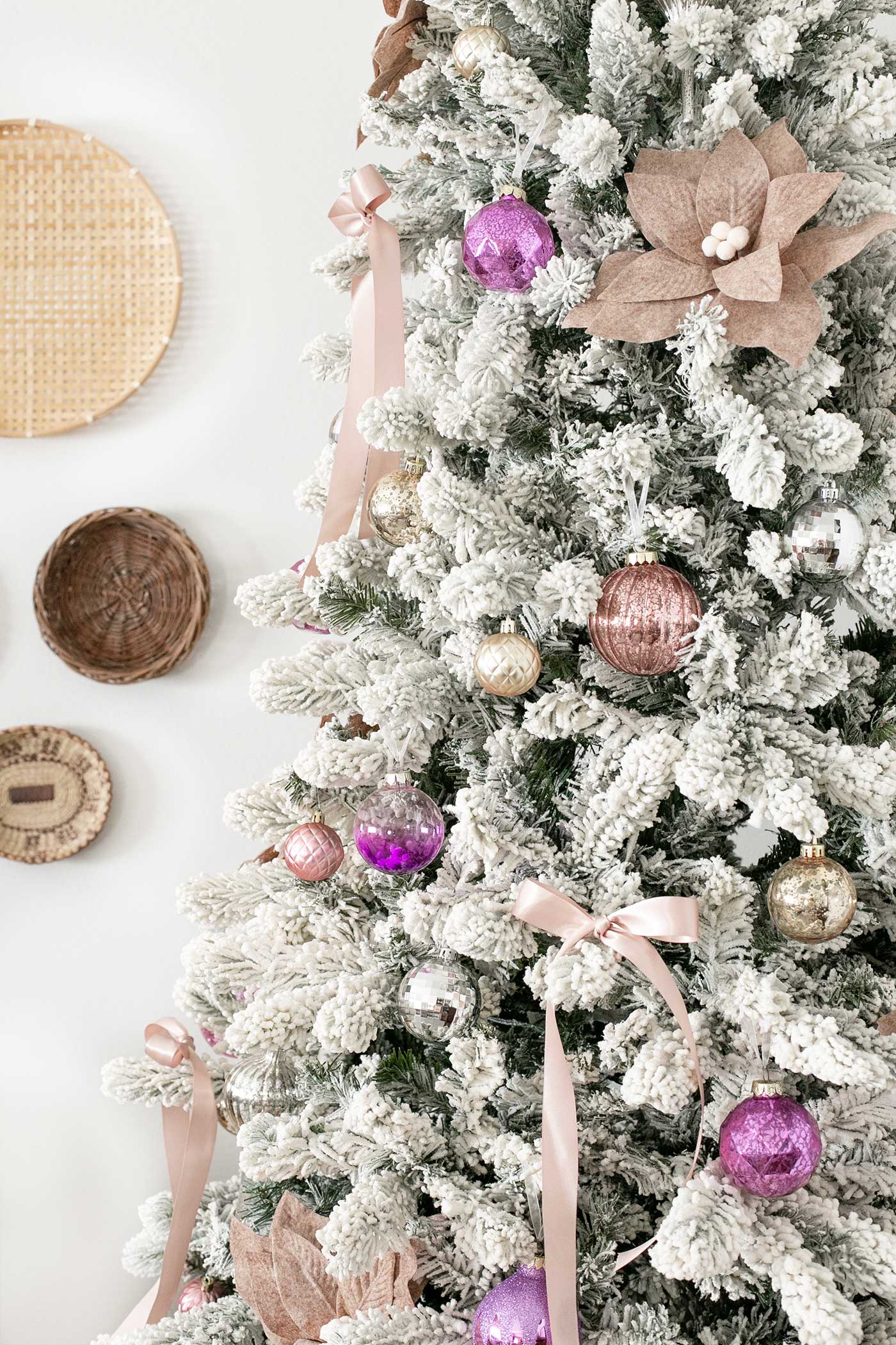 Blush holiday decor with a slim flocked tree and natural basket wall accents.