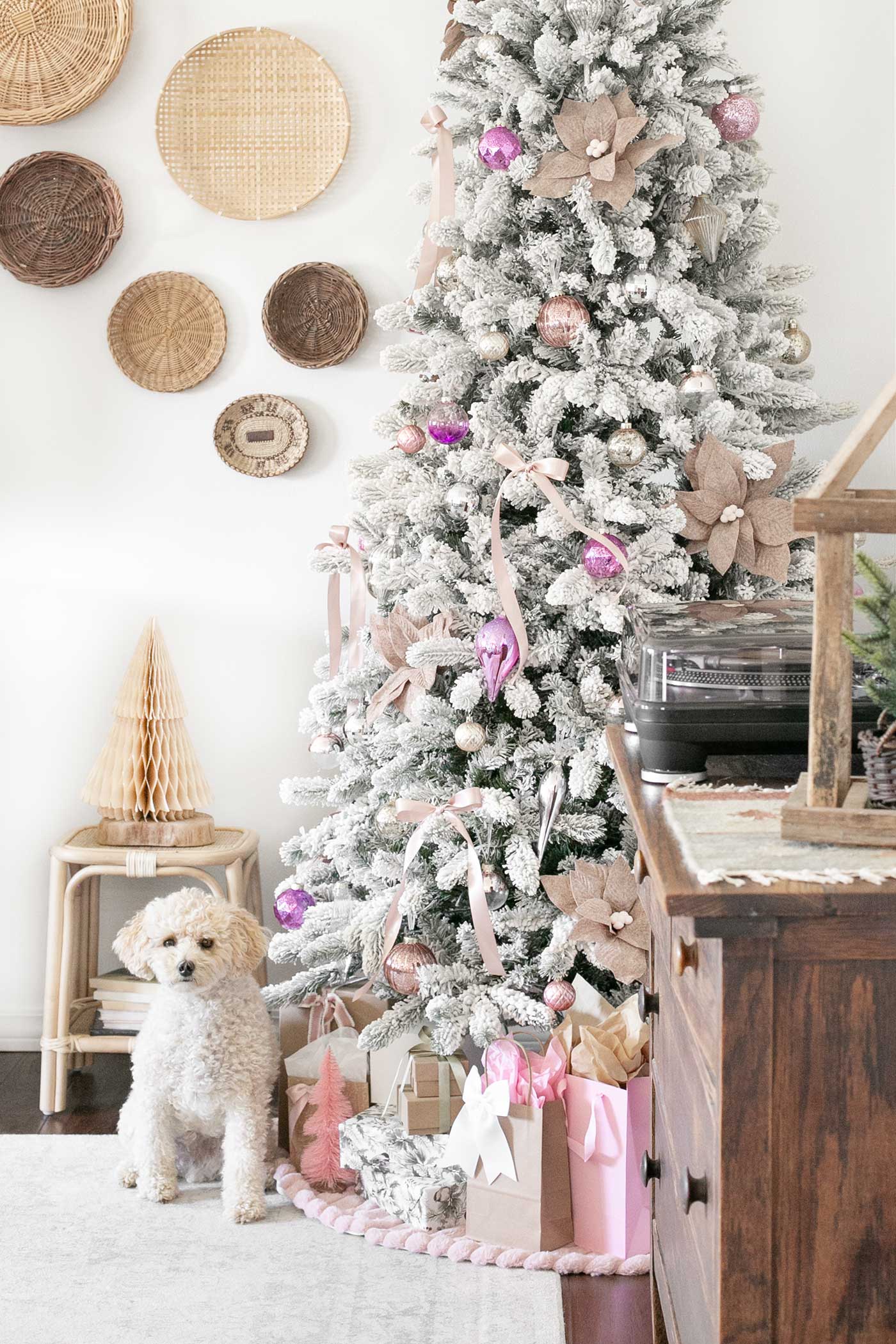 Dog sitting near gifts under a flocked Christmas tree decorated in soft pretty in pink tones.