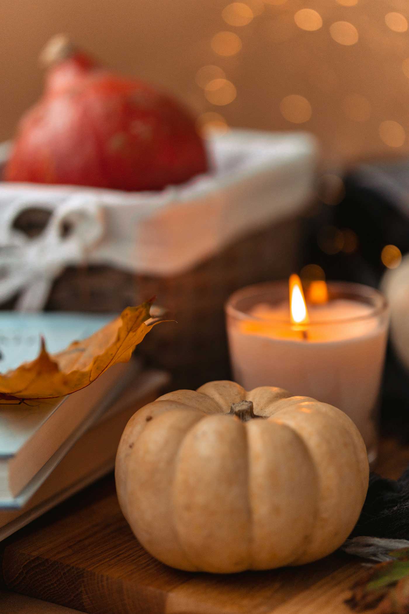 Cream mini pumpkin and lit candle styled with autumn leaves and warm fall décor on a wooden surface.