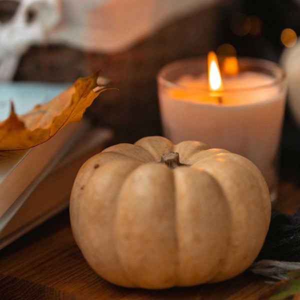 Cream mini pumpkin and lit candle styled with autumn leaves and warm fall décor on a wooden surface.