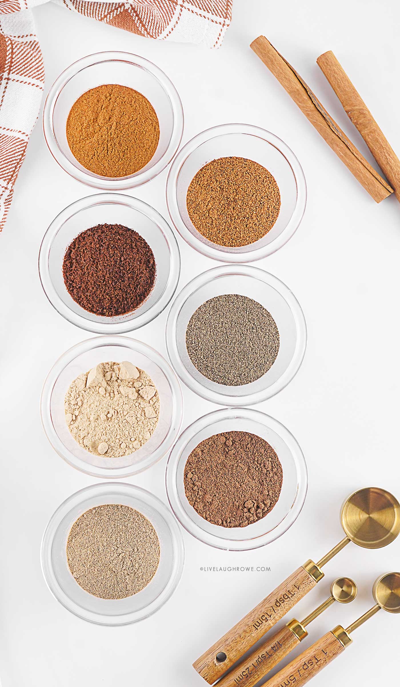 Beautiful flat lay of spices — cinnamon sticks, ground cardamom, ginger, and nutmeg — laid out on parchment paper for making a recipe.