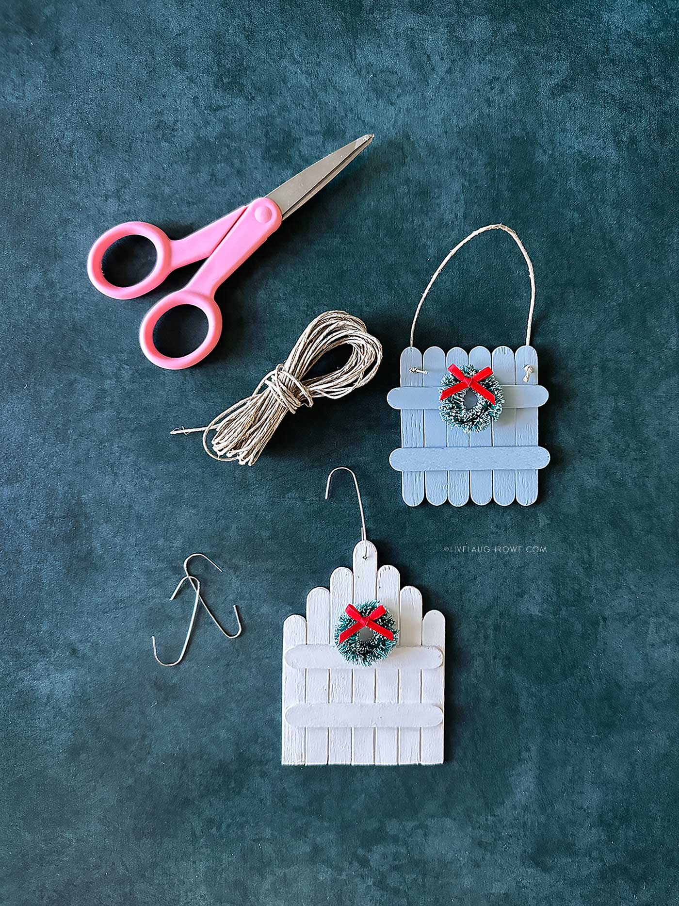 Pink scissors, twine, and hooks displayed with ornaments in pastel colors.